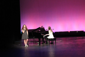 Julia Foran and Talitha Jones, on piano, sing a duet to the song “Wrecking Ball”. 