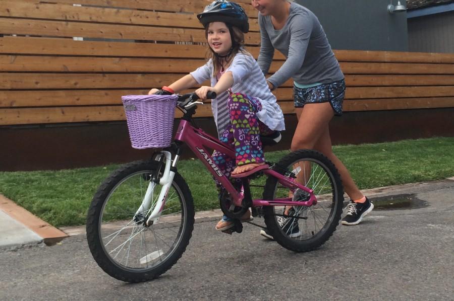 High school babysitter helping a first grader ride her bike over the summer.