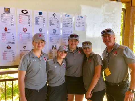 A few members of the golf team and the coach pose for a picture in front of the score board.