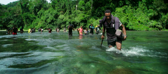 People crossing a river as part of the journey through the Darien Gap.