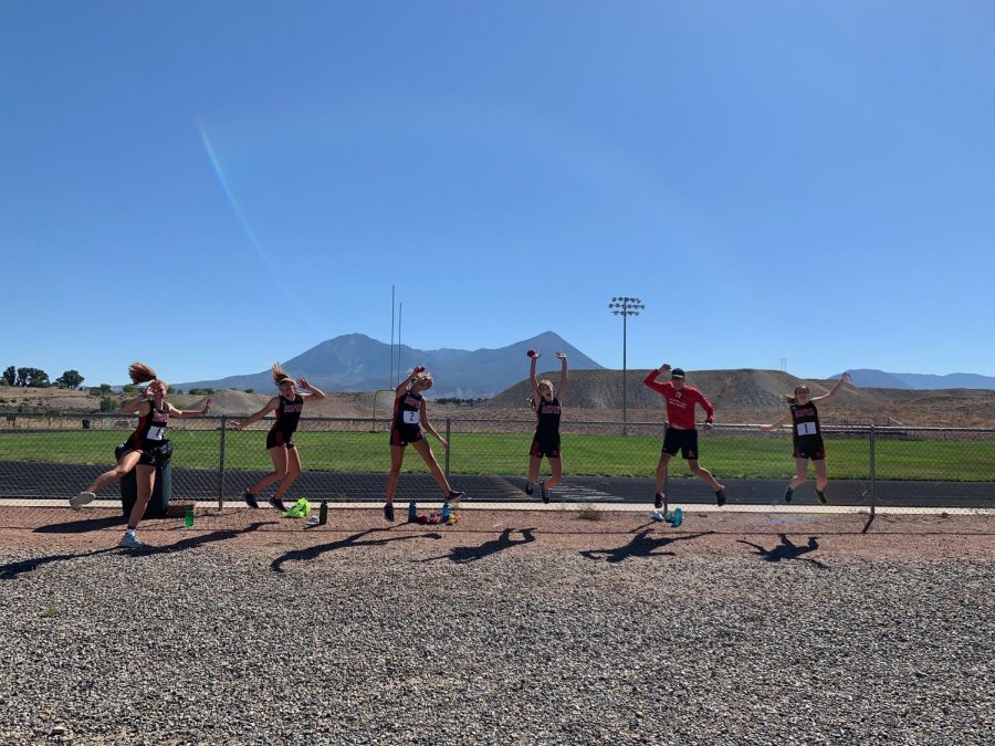 Runners (from left) Edie Sherlock, Stella Sherlock, Kylie Kenny, Michaela Kenny, Coach Chris Keleher, and Macy Hopkinson jump for joy after their Hotchkiss race.   