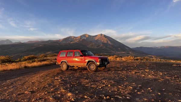 A gorgeous photo of the bright yellow sunrise hitting a 1996 Jeep Cherokee; with Mt. Sopris brightening up the gorgeous landscape behind it.