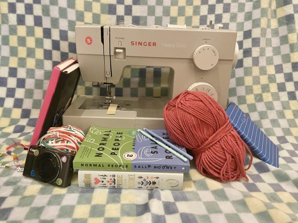 An array of hobby materials, including journals, yarn, a Kindle, a camera, books, and a sewing machine. 