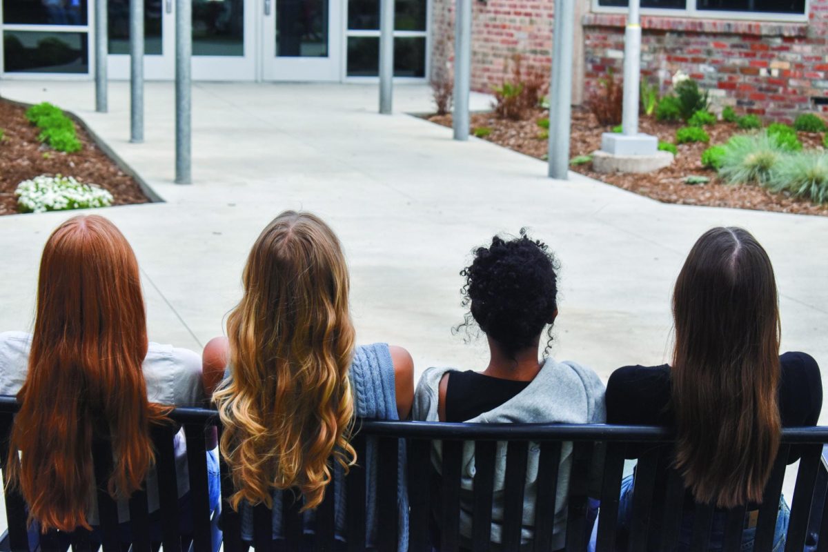 Three girls with all different hair colors and textures sit on a bench.