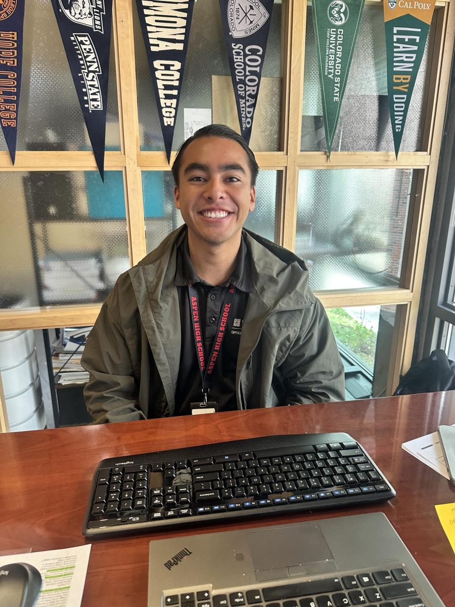Mateo Leaño smiles for the camera in his post-secondary counseling office, surrounded by flags of where students have committed to college.